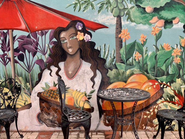 Colorful mural of a black hispanic woman in a tropical setting with cafe seating
